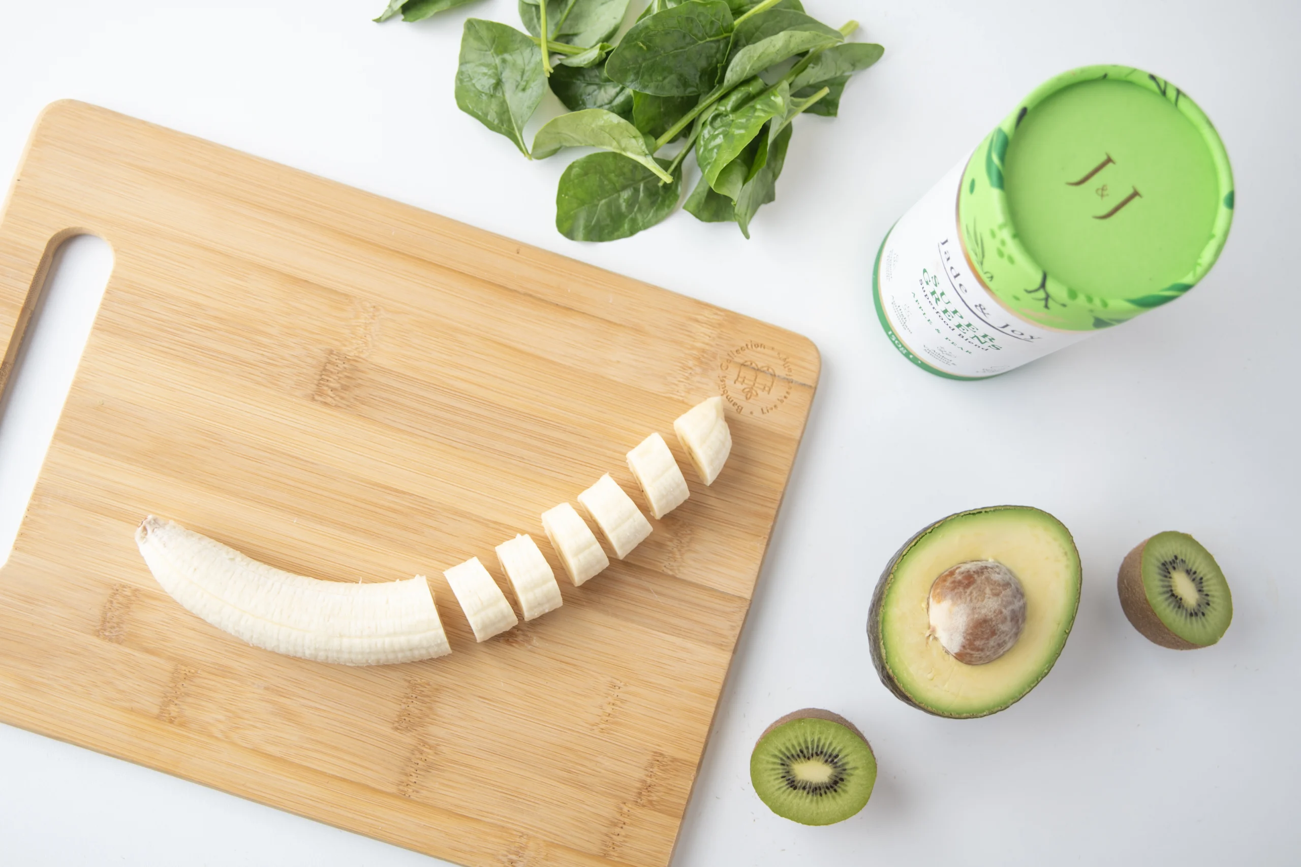 Ingredients for a super greens smoothie: chopped banana, kiwi, avocado, spinach and Jade & Joy Super Greens powder