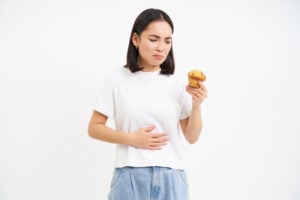 portrait asian woman with stomach ache holding cupcake food poisoning feeling unwell studio backg