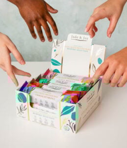Hands reaching towards Jade & Joy bespoke collagen protein bars box